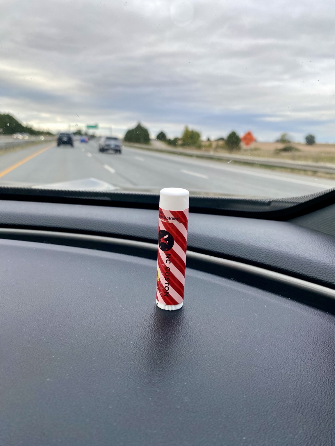 An NC Custom lip balm on a car dashboard with the open road in the background